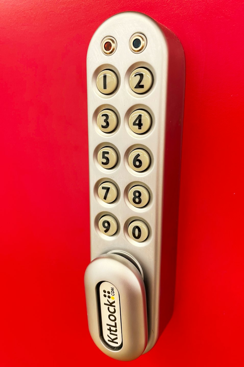 Silver keypad lock with large cream number buttons on red surface.