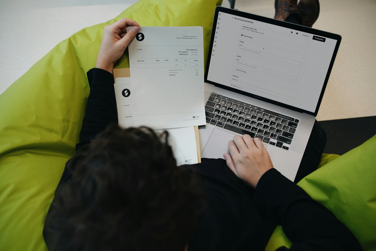 Person reviews invoice on laptop while sitting on a bean bag.